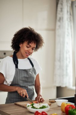 Önlüklü, havuç kesen ve mutfakta yemek hazırlayan çekici melez bir kadın. Mutfak tezgahında sebze var..