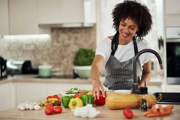 Vacker blandras hemmafru sträcker sig efter röd paprika när du står i köket. Middagstillagning. — Stockfoto