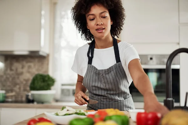 Bela dona de casa de raça mista chegando para o pimentão verde enquanto está na cozinha. Preparação para jantar . — Fotografia de Stock