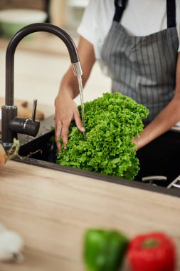 Mutfak lavabosunda marul yıkayan melez bir kadın. Yemek hazırlama konsepti.