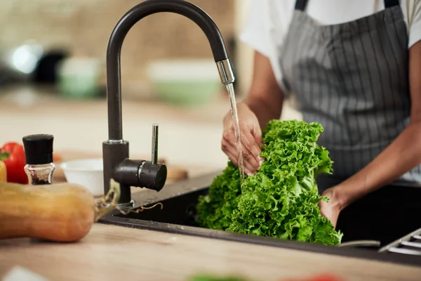 Mujer de raza mixta lavando lechuga en fregadero de cocina. Concepto de preparación de comidas . — Foto de Stock