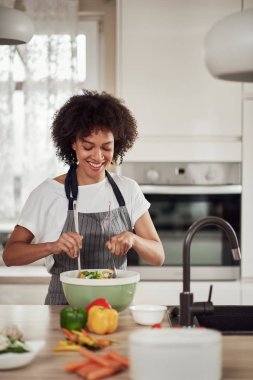 Önlüklü, kıvırcık saçlı, evde mutfakta sebze karıştıran çekici bir ırk kadını..