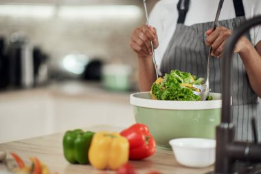 Önlüklü çekici melez kadın mutfakta dururken kasede sebze karıştırıyor..