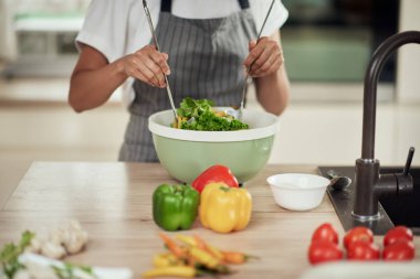 Önlüklü çekici melez kadın mutfakta dururken kasede sebze karıştırıyor..