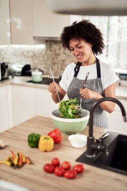 Önlüklü çekici melez kadın mutfakta dururken kasede sebze karıştırıyor..