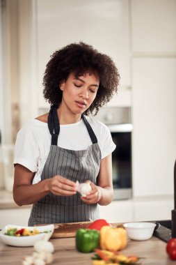 Önlüklü muhteşem melez kadın mutfakta duruyor ve sarımsak soyuyor..