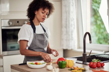 Önlüklü muhteşem melez kadın mutfakta duruyor ve sarımsak soyuyor..