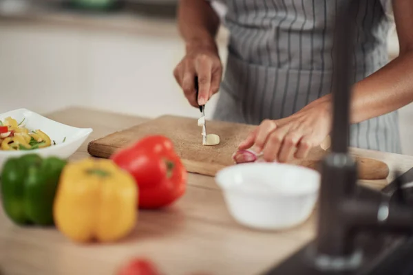 Primer plano de la mujer de raza mixta en delantal de pie en la cocina doméstica y cortar el ajo . — Foto de Stock