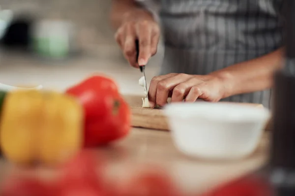 Primer plano de la mujer de raza mixta en delantal de pie en la cocina doméstica y cortar el ajo . — Foto de Stock