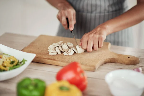 Close-up van gemengde race vrouw in schort staand in de keuken en het hakken van paddestoelen. — Stockfoto