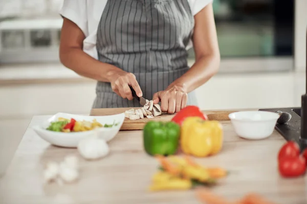 Close up de mulher de raça mista em avental de pé na cozinha e cortando cogumelos . — Fotografia de Stock