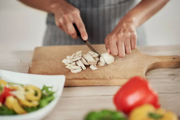 Primer plano de la mujer de raza mixta en el delantal de pie en la cocina y cortar setas . — Foto de Stock