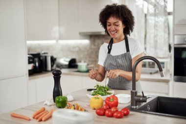 Önlüklü çekici melez kadın mutfakta dururken kasede sebze karıştırıyor..