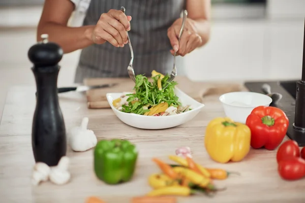Close-up van gemengde ras vrouw in schort mengen groenten in kom terwijl staan in de keuken thuis. — Stockfoto