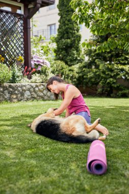 Genç, çekici, formda bir Yogi esmer arka bahçede köpeğiyle oynuyor..