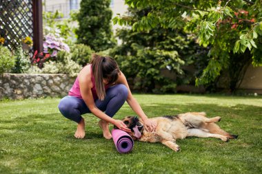 Genç, çekici, formda bir Yogi esmer arka bahçede köpeğiyle oynuyor..