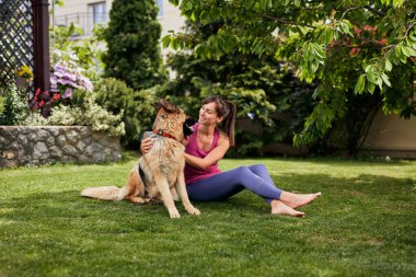 Genç, çekici, formda bir Yogi esmer arka bahçede köpeğiyle oynuyor..