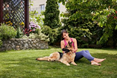 Genç, çekici, formda bir Yogi esmer arka bahçede köpeğiyle oynuyor..