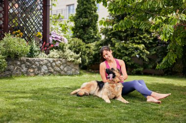 Genç, çekici, formda bir Yogi esmer arka bahçede köpeğiyle oynuyor..