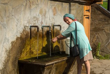 Yaz güneşli gününde su musluğu altında bir elma yıkama yaşlı gülümseyen kadın
