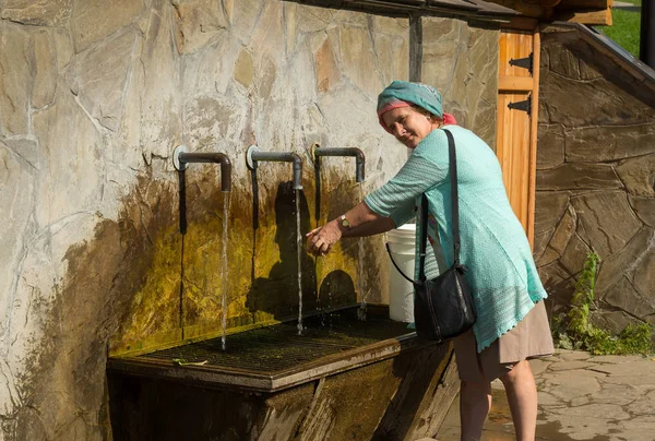 Yaz güneşli gününde su musluğu altında bir elma yıkama yaşlı gülümseyen kadın