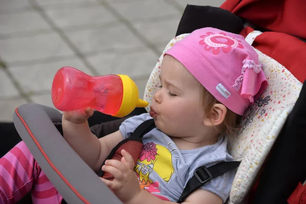 Bebek arabasındaki küçük kız yaz yürüyüşünde şişeden su içer. 