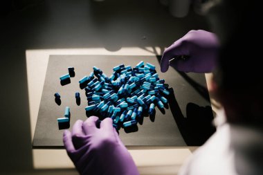 Mavi kapsüllerle çalışan bir bilim adamının elleri.