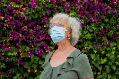 Sokakta mavi cerrahi maske takan yaşlı bir kadın.