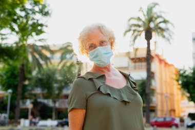 Sokakta mavi cerrahi maske takan yaşlı bir kadın.