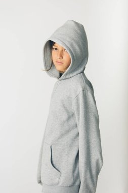 Beyaz arka planda duran kapüşonlu kazaklı 11 yaşında bir çocuk.