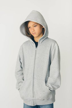 Beyaz arka planda duran kapüşonlu kazaklı 11 yaşında bir çocuk.