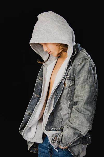 Siyah arka planda duran kapüşonlu kazaklı ve kot ceketli 11 yaşında bir çocuk.