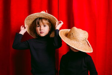 Siyah giysili iki çocuk ve kırmızı bir perdeye karşı saman kulübesi.