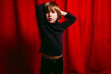 Beş yaşında bir çocuk, kırmızı bir perdeye karşı.