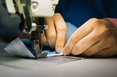 Bir terzinin elleri dikiş makinesiyle tıbbi giysiler dikiyor.
