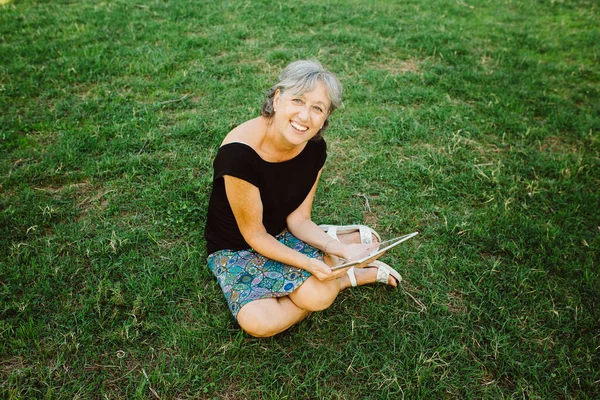 Senior woman chatting on-line with his tablet in a park