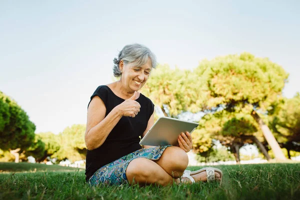 Senior woman chatting on-line with his tablet in a park