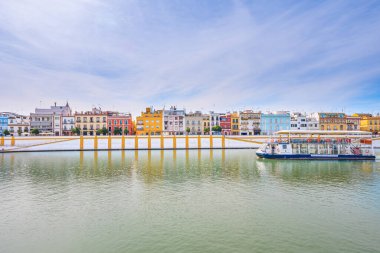 Sevilla, İspanya. 15 Ekim 2019. Guadalquivir nehrinin kıyısındaki Calle Betis 'in renkli evlerinin manzarası. Bir tekne Guadalquivir Nehri seyahati yapar.