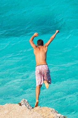Lefkada, Yunanistan. 18 Ağustos 2011. Yunanistan 'ın Lefkada kentindeki Agios Ioannis körfezinde bir çocuk kayadan turkuaz bir denize atlar..