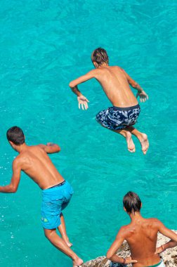 Lefkada, Yunanistan. 18 Ağustos 2011. Bazı çocuklar Yunanistan 'ın Lefkada kentindeki Agios Ioannis körfezinde bir kayadan turkuaz denize atlıyorlar..