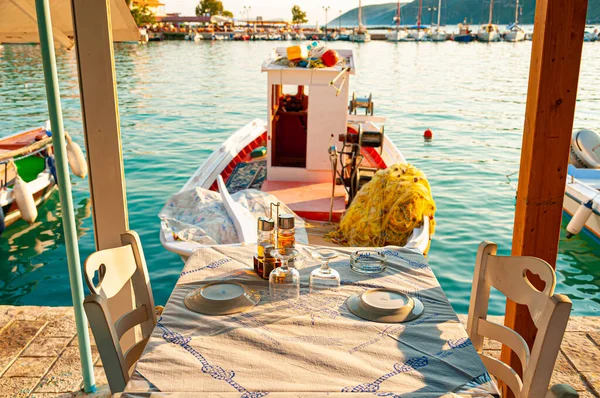 Lefkada, Yunanistan. 18 Ağustos 2011. Vassiliki Körfezi. Rıhtıma yanaşmış balıkçı teknesi olan deniz kenarında bir restoranın masası..