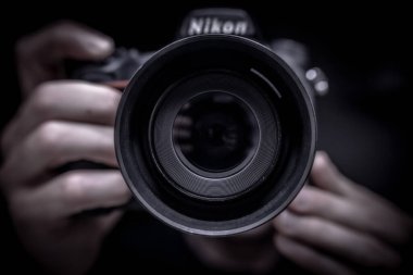 Naples, Italy. July 22th, 2019. A person holds a nikon. Hands hold a nikon. A Nikon camera reflected in the mirror. Taking  photo of yourself at the mirror. Close-up of a photographic lens. clipart