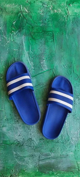 Pair of blue slippers with white bands on a green backdrop.