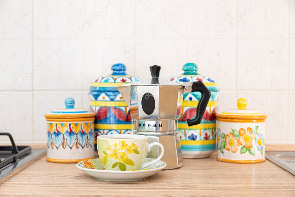 Italy. A cup of coffee and a coffee pot placed in front of pretty and colorful Vietri ceramic jars on the kitchen counter.