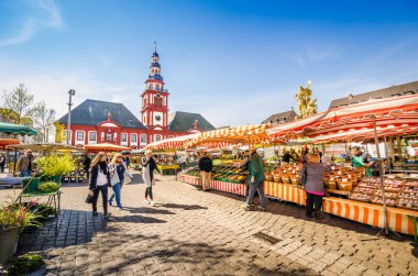 Mannheim, Almanya. 27 Mart 2014. Güneşli bir günde insanlar yiyecek stantları arasındaki pazar meydanında yürürler ve taze yerel ürünler almak için dururlar..