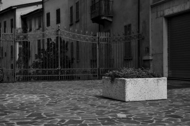 Demir kapının yanındaki bir meydanda beton işçisi ve siyah ve beyaz bir bina.