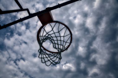 Aşağıdan görülen bir basketbol potası, bulutlu bir gökyüzü arka grup olarak görülüyor.