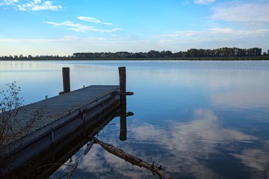 Gün batımında göl kıyısında, gökyüzü suya gömülmüş.