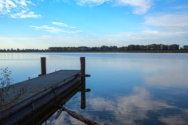 Gün batımında göl kıyısında, gökyüzü suya gömülmüş.