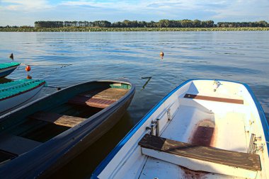 Gün batımında bir gölün kıyısında demirlemiş tekneler.
